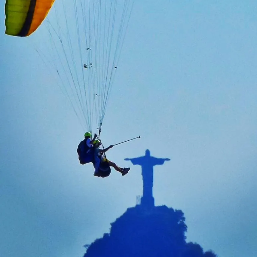 Casal em voo de parapente sobre Niterói com o Cristo ao fundo
